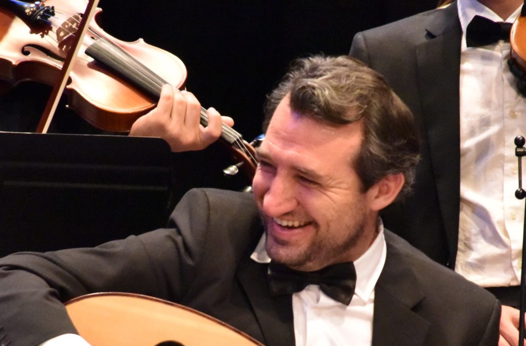 Development Director Miles Markstein smiles to right of frame holding a guitar.